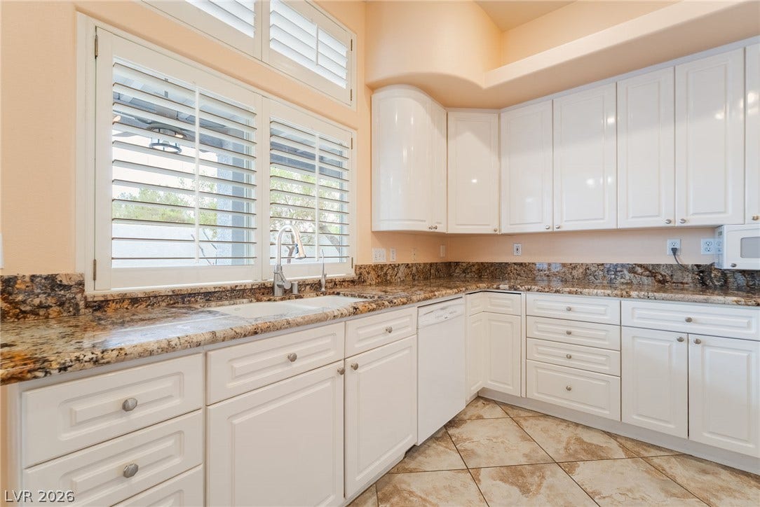 3775 Rick Stratton Drive, Las Vegas, NV 89120 A well-lit kitchen boasts elegant white cabinetry, durable granite countertops, and a double sink, ready for culinary endeavors.