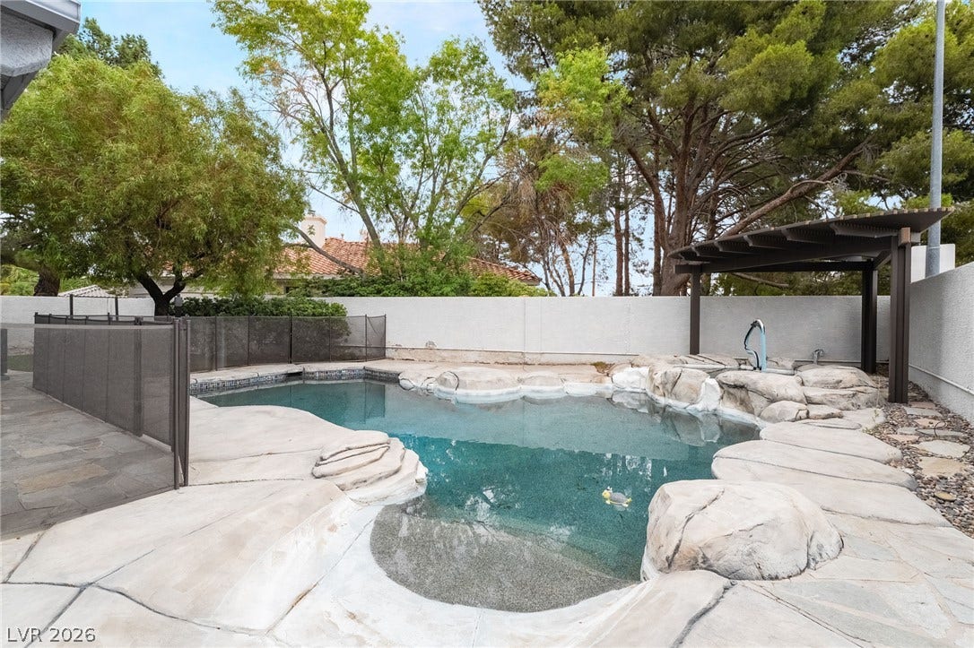 3775 Rick Stratton Drive, Las Vegas, NV 89120 A tranquil backyard oasis features a rock-lined pool, shaded pergola, and private fencing.