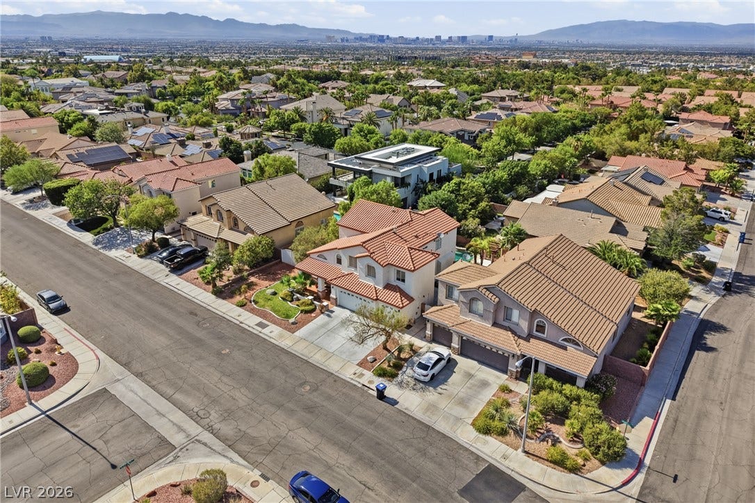 2218 Alanhurst Drive, Henderson, NV 89052 An aerial perspective reveals a vibrant neighborhood with diverse rooflines and lush landscaping, all set against a distant cityscape.