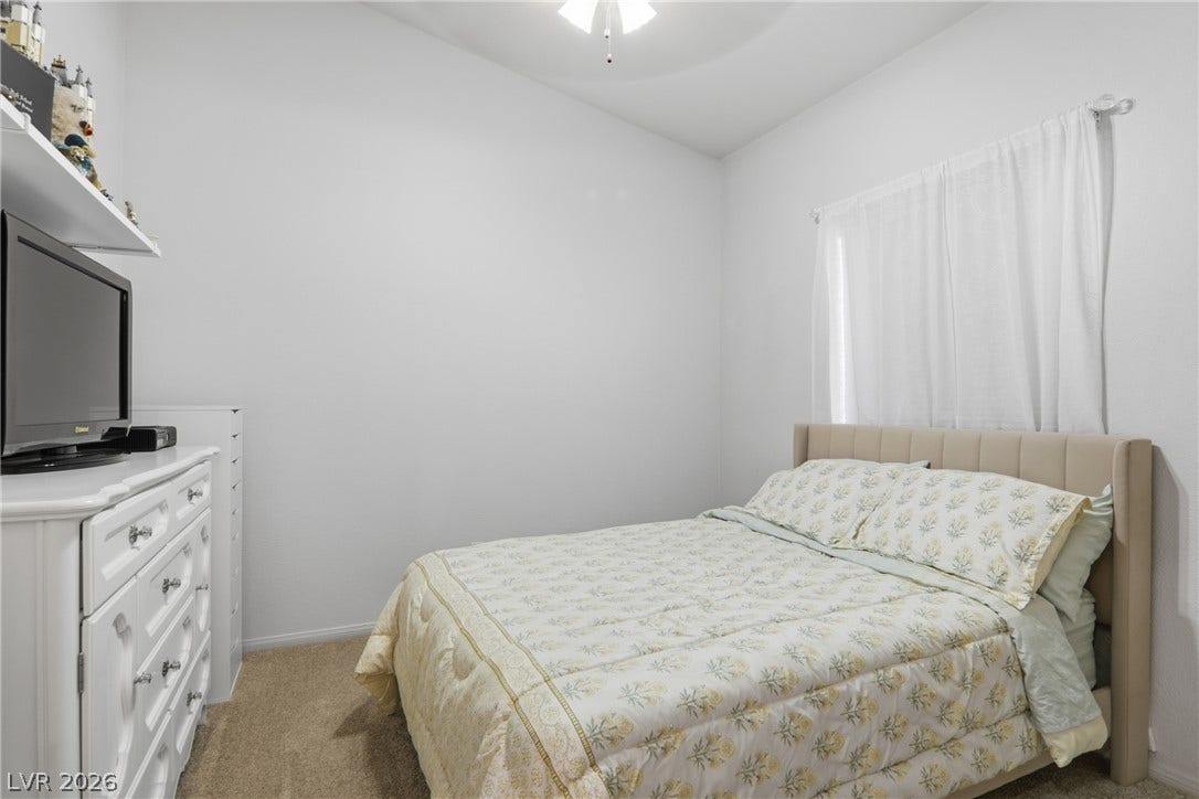 2218 Alanhurst Drive, Henderson, NV 89052 A cozy bedroom features soft carpeting, a ceiling fan, and ample natural light from a well-placed window.