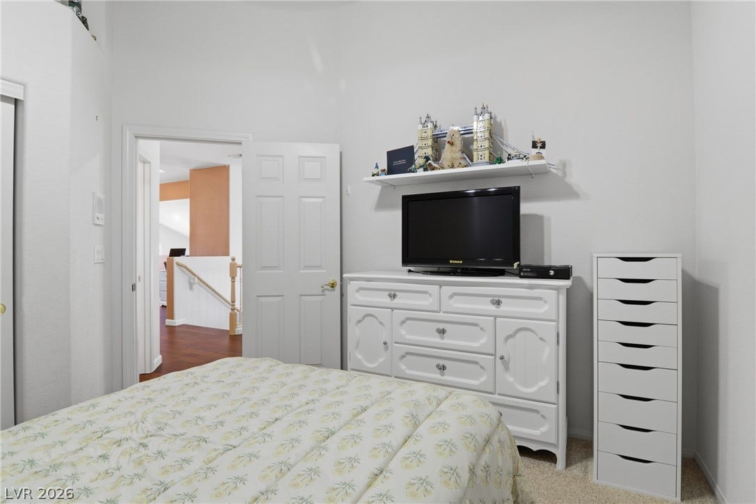 2218 Alanhurst Drive, Henderson, NV 89052 Bedroom featuring a light-toned carpet and a view into a hallway with hardwood flooring and a classic wooden banister.
