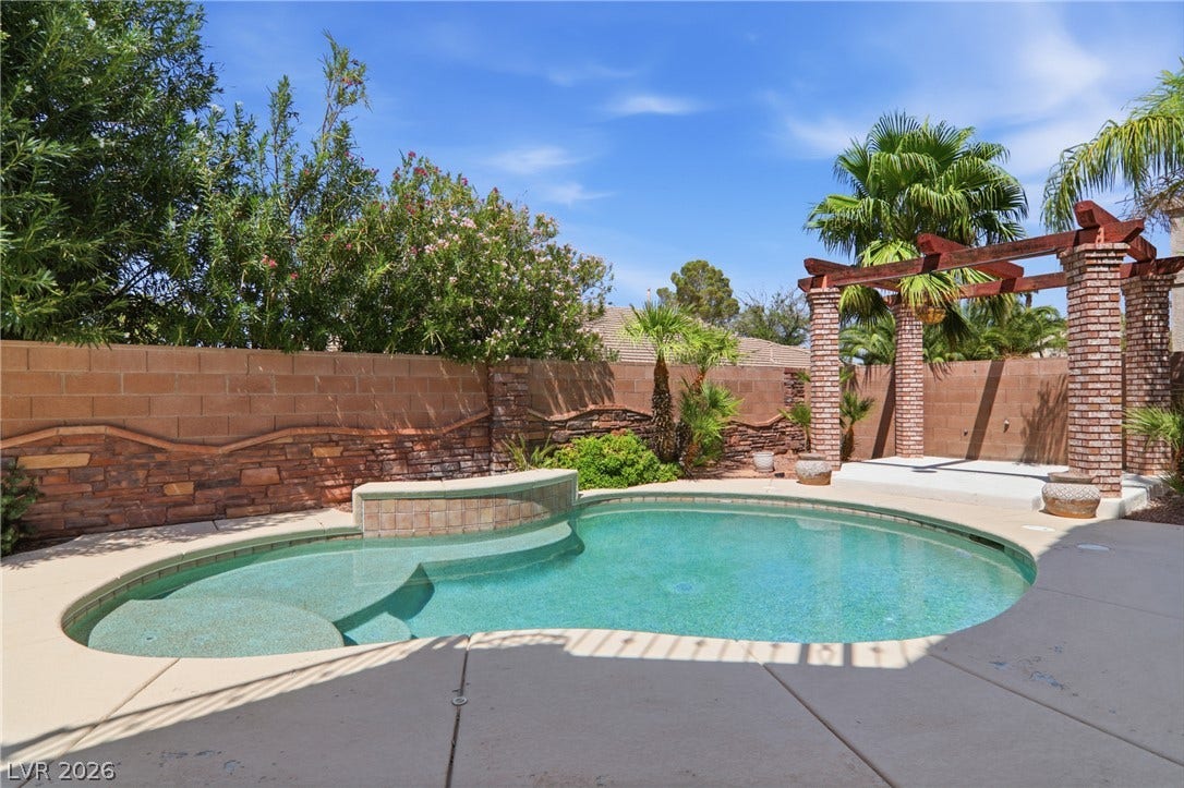 2218 Alanhurst Drive, Henderson, NV 89052 A private backyard oasis features a free-form pool and spa, complemented by a decorative brick pergola and lush greenery.