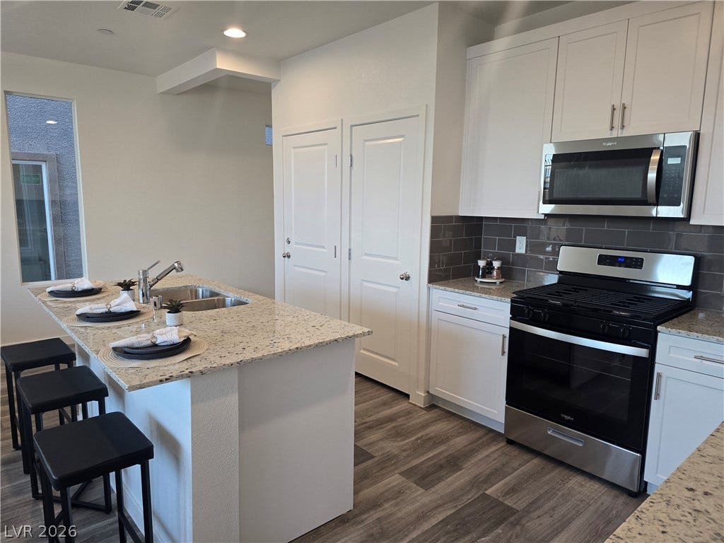 4926 Sweet Vesper Court, Las Vegas, NV 89108 An inviting kitchen features a stone-topped island, gas range, and warm wood flooring.
