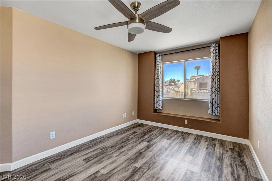 8308 Raphael Court, Las Vegas, NV 89129 A well-lit bedroom with modern wood-style flooring features a large window overlooking the neighborhood and a functional ceiling fan.