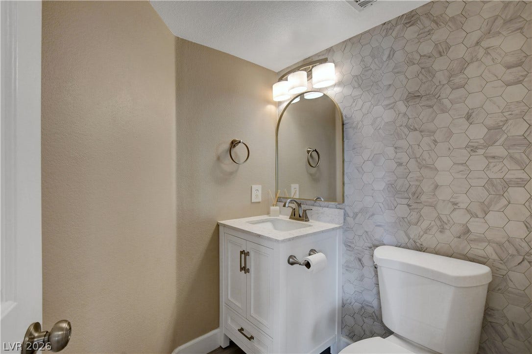8308 Raphael Court, Las Vegas, NV 89129 A chic powder room features a modern vanity with a marble countertop, complemented by a striking hexagonal tiled accent wall.