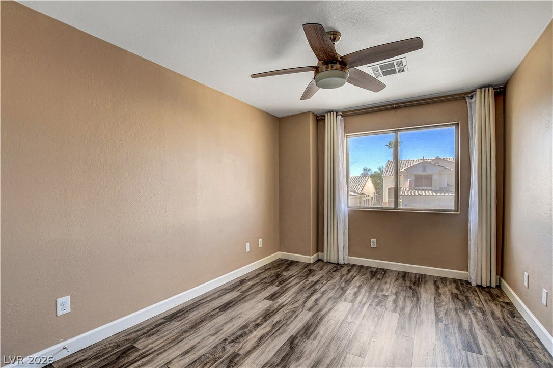 8308 Raphael Court, Las Vegas, NV 89129 Well-lit room features a ceiling fan, a window with outdoor views, and wood flooring.