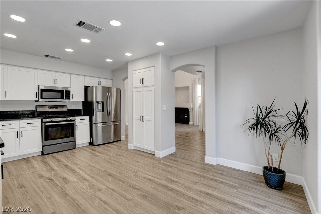 8308 Raphael Court, Las Vegas, NV 89129 A well-appointed kitchen features stainless steel appliances and abundant white cabinetry, seamlessly connecting to an adjoining living space.