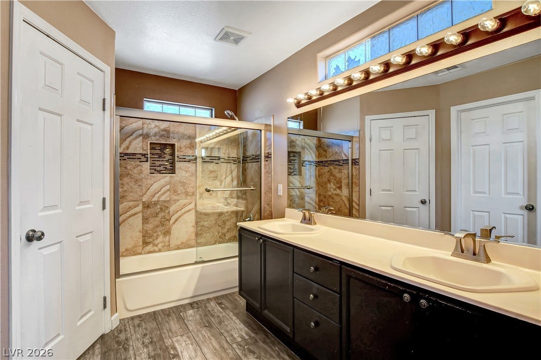8308 Raphael Court, Las Vegas, NV 89129 Dual vanities complement a tiled shower and tub in this inviting bathroom space.