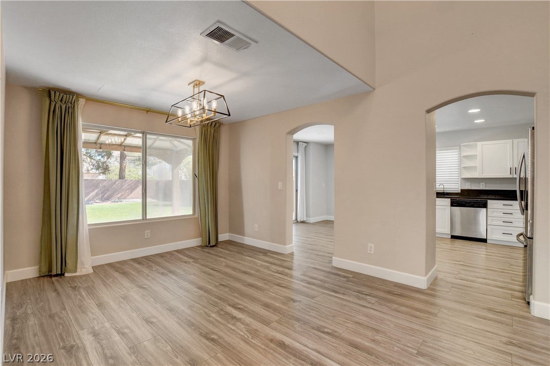 8308 Raphael Court, Las Vegas, NV 89129 A luminous dining area with a modern chandelier and inviting views of the yard, flowing seamlessly into a well-appointed kitchen.