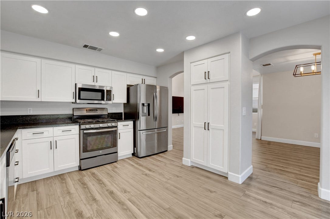 8308 Raphael Court, Las Vegas, NV 89129 White cabinetry, dark stone countertops, and wood flooring define this kitchen's appealing aesthetic.