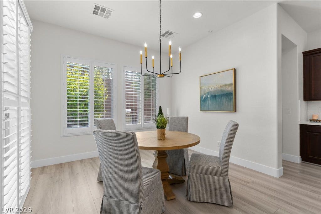 2828 Josephine Drive, Henderson, NV 89044 A refined dining space features a sleek black chandelier above a round wooden table, illuminated by multiple windows.