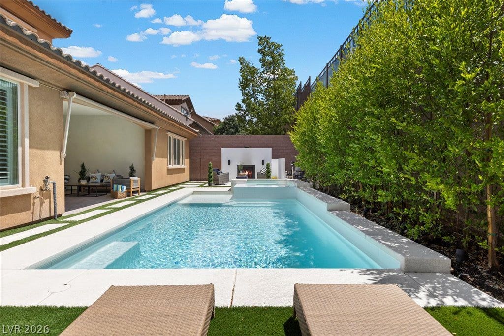 2828 Josephine Drive, Henderson, NV 89044 An inviting backyard oasis offers a sparkling pool with an integrated spa, bordered by lush greenery and a cozy outdoor fireplace.