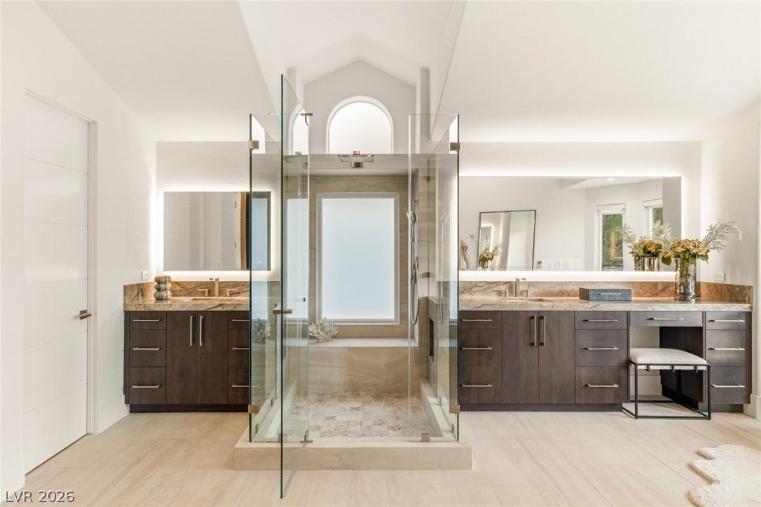 Luxurious primary bath with dual vanities, a spacious glass shower, and elegant tile flooring.