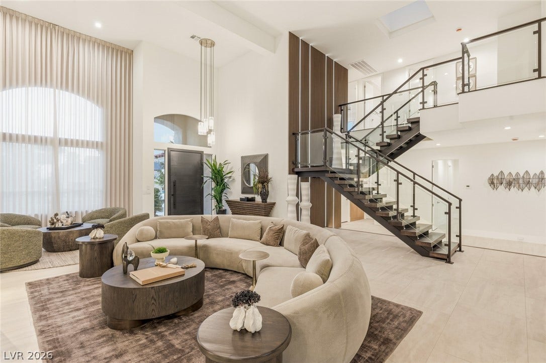 A grand entrance with high ceilings, modern glass railings on the staircase, and luminous tile flooring throughout.