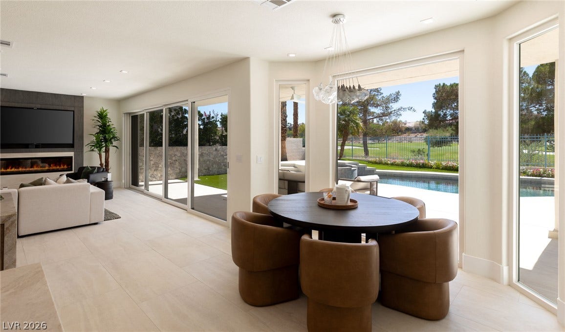 Seamless indoor-outdoor living with elegant flooring, an inviting fireplace, and sliding glass doors revealing a refreshing pool and green views.