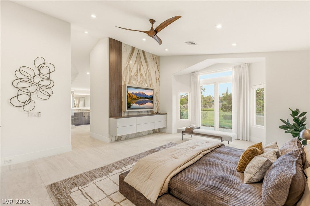 A spacious primary bedroom with a contemporary ceiling fan and views of lush greenery.