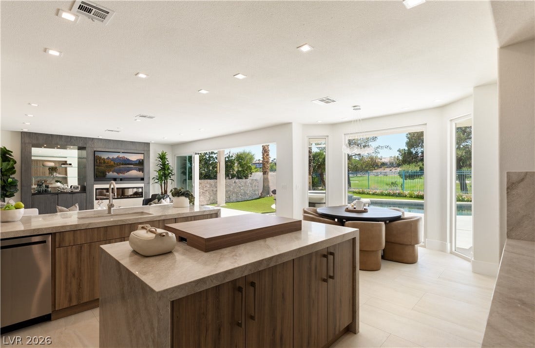 A well-lit kitchen with modern wood cabinetry and stone countertops overlooks a lush golf course and swimming pool.