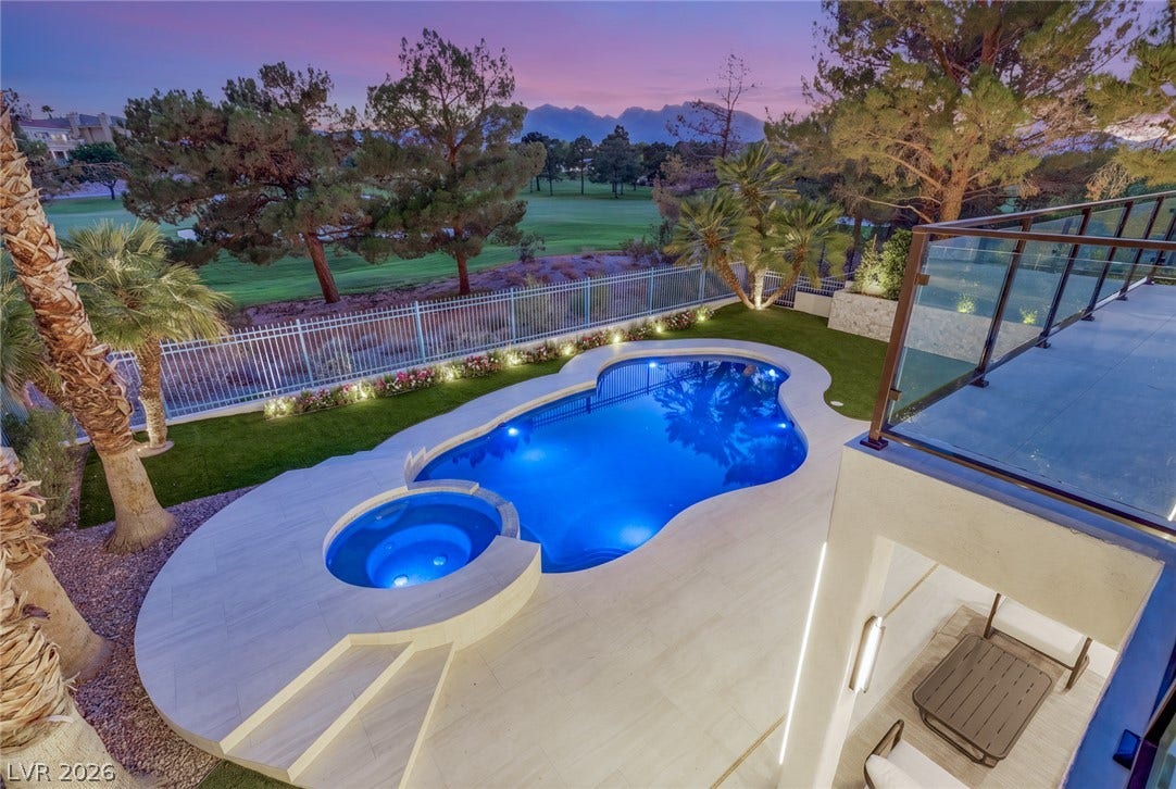 An illuminated backyard pool and spa offer a tranquil oasis overlooking a green golf course.