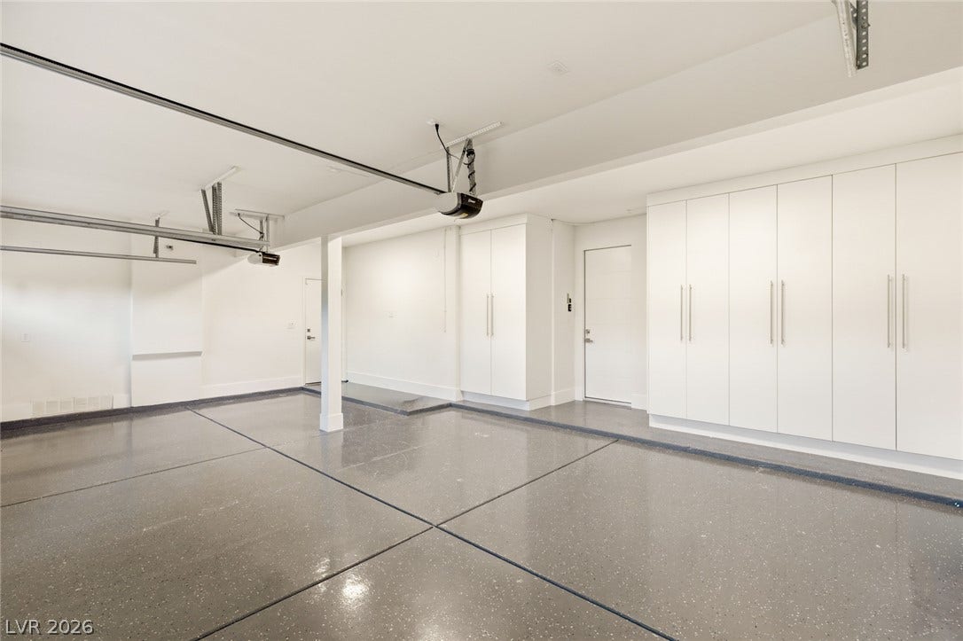 A spotless garage boasts a durable, speckled epoxy floor and ample, clean-lined white cabinetry for organized storage.