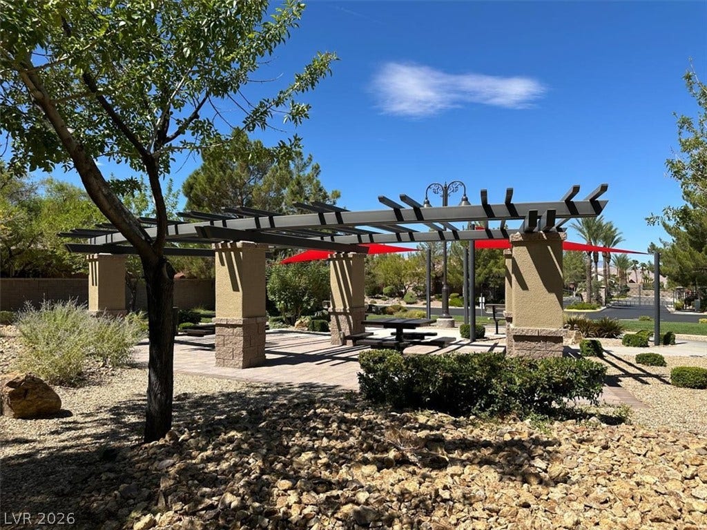 An outdoor shade structure sits within a landscaped common area under clear skies.