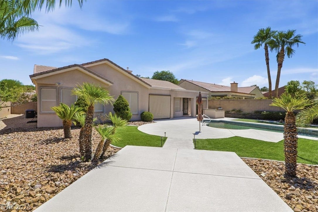 A spacious concrete patio borders a private pool and manicured lawn under clear desert skies.