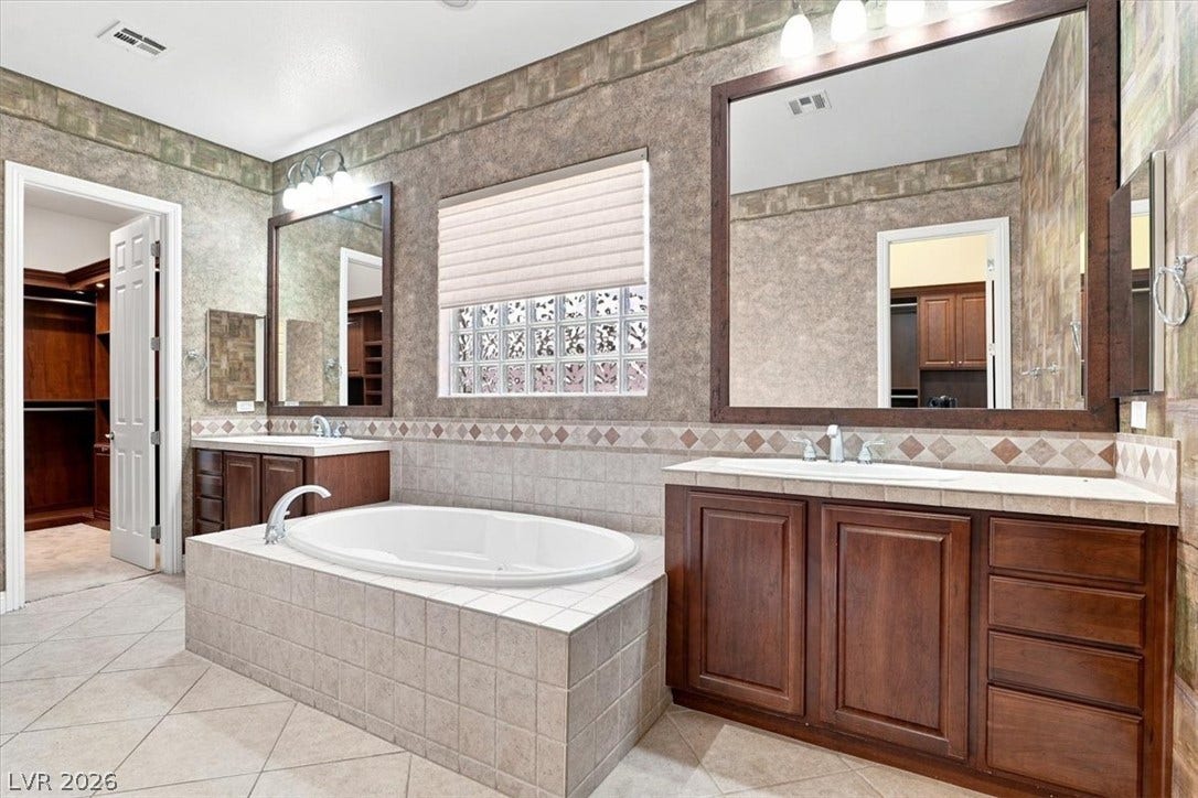 Tiled flooring and matching vanities flank a central soaking tub under high ceilings.