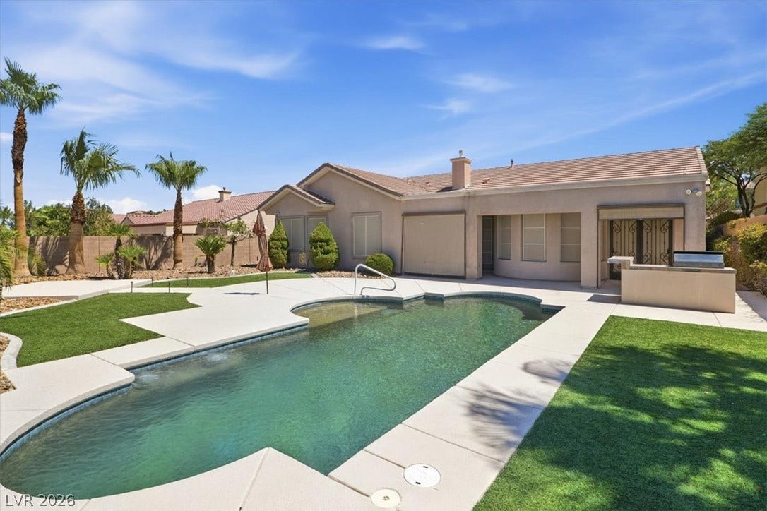 An inviting backyard pool is bordered by manicured lawn areas and a stucco exterior.