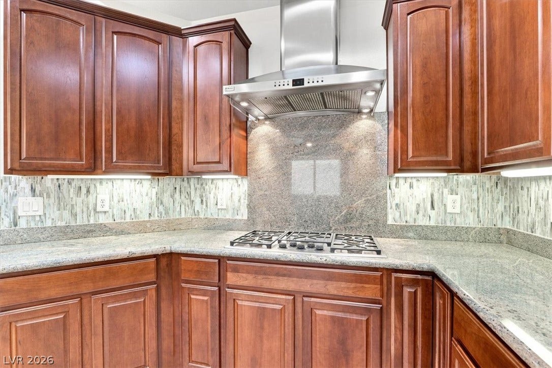 Rich wood cabinetry surrounds a stone cooktop area complete with a sleek professional range hood.