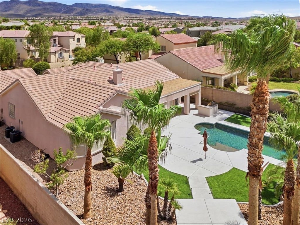Palm trees frame a stone tile roof residence overlooking an in-ground swimming pool.