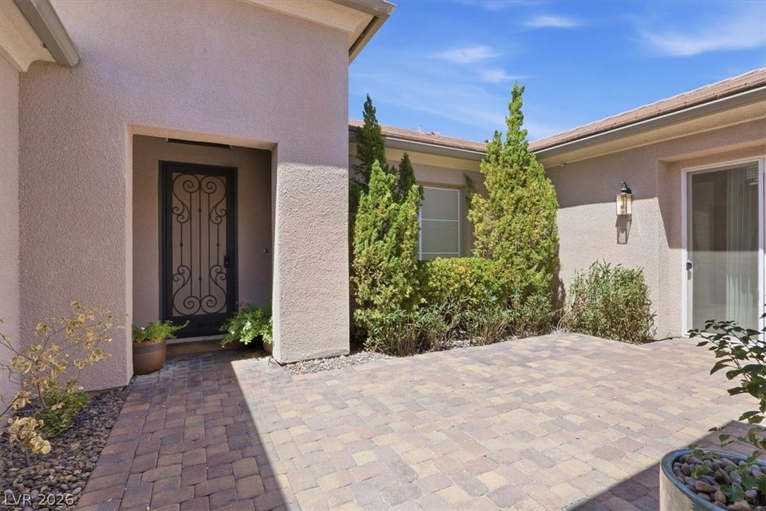 An inviting stone-paved entry courtyard features a detailed glass door and stucco walls.