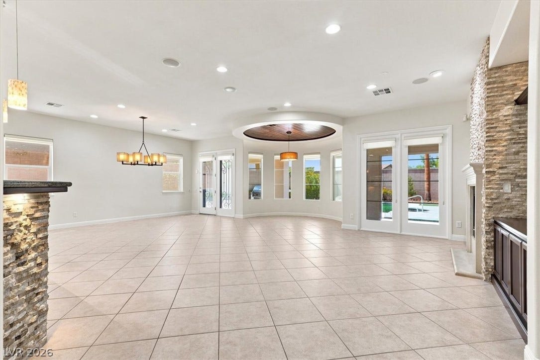 A spacious layout features tiled flooring, a stone-faced fireplace, and a tray ceiling details.