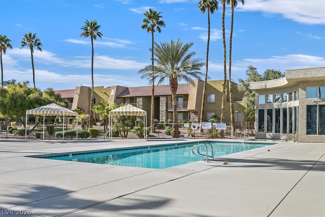 5081 River Glen Drive, #97, Las Vegas, NV 89103 Lush palm trees surround a sparkling blue swimming pool set against modern desert-inspired architecture.