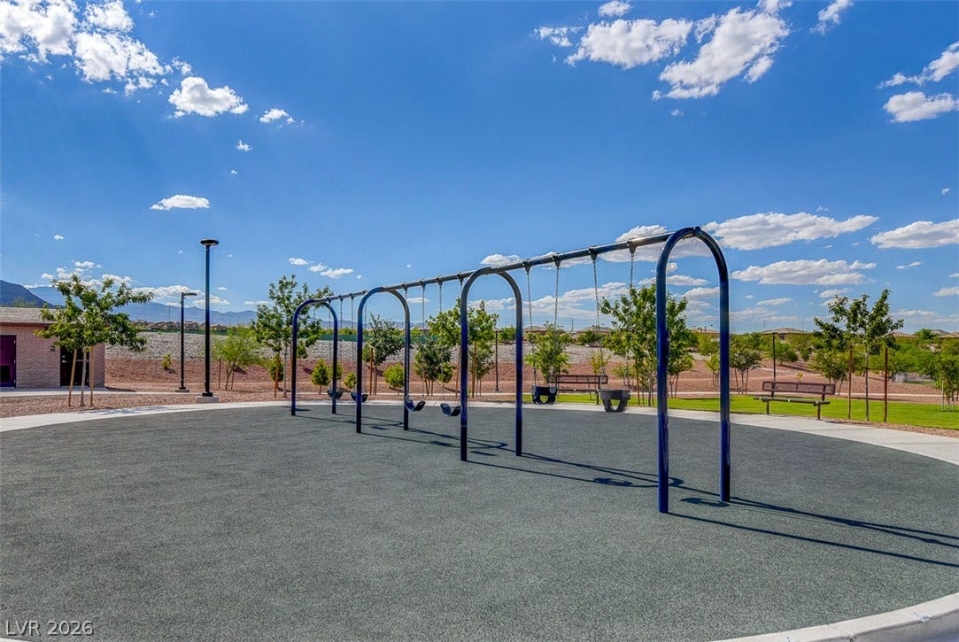9928 Tradition Creek Avenue, Las Vegas, NV 89149 A community playground featuring a swing set, mature trees, and a mountain backdrop for outdoor enjoyment.
