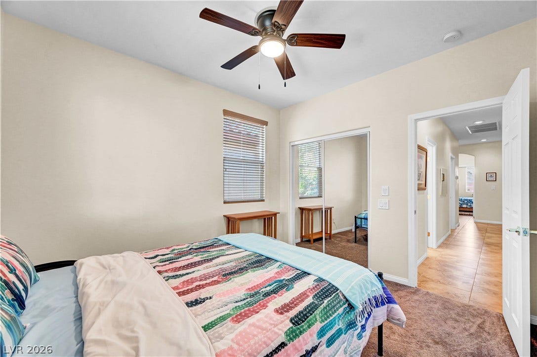 9928 Tradition Creek Avenue, Las Vegas, NV 89149 A well-lit bedroom provides comfortable repose, with a ceiling fan enhancing airflow and mirrored closet doors creating an illusion of space.