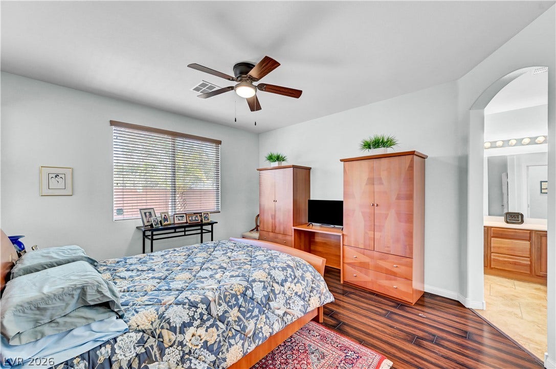 9928 Tradition Creek Avenue, Las Vegas, NV 89149 Well-lit sleeping quarters with rich wood flooring and a contemporary ceiling fan, offering a clear view into the adjacent bath.