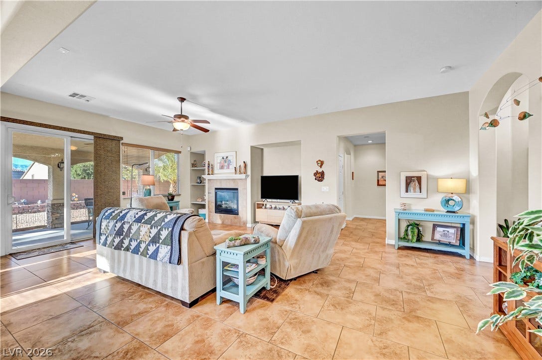 9928 Tradition Creek Avenue, Las Vegas, NV 89149 A well-lit living area features tiled flooring, a cozy fireplace, and direct access to an outdoor patio.