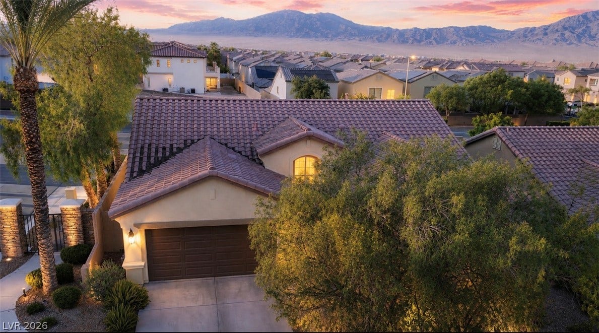9928 Tradition Creek Avenue, Las Vegas, NV 89149 A terracotta tile roof crowns this inviting home, set against a distant mountain range and a vibrant sunset sky.