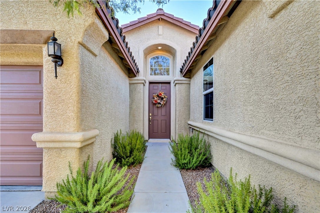 9928 Tradition Creek Avenue, Las Vegas, NV 89149 A welcoming entry features a dark wood door with an arched transom, flanked by verdant landscaping.