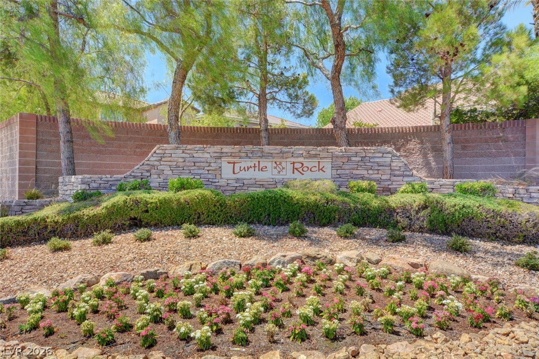 9928 Tradition Creek Avenue, Las Vegas, NV 89149 A welcoming stone-clad entrance sign for "Turtle Rock" community is framed by verdant shrubs, mature trees, and a vibrant flower bed.