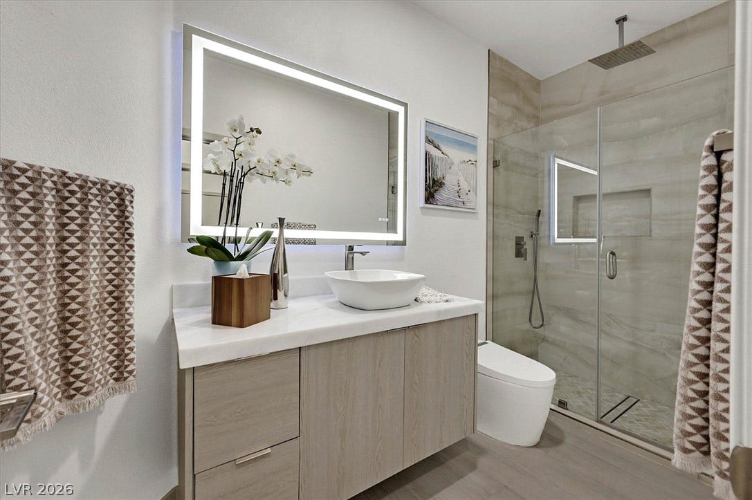 A well-appointed bathroom offers a vanity with a vessel sink and an illuminated mirror alongside a glass-enclosed shower.