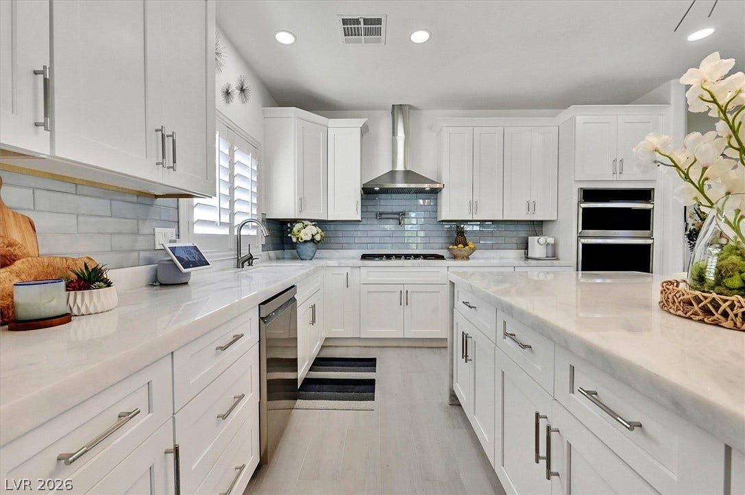 White cabinetry, sleek countertops, and modern appliances outfit this luminous, open-concept kitchen.