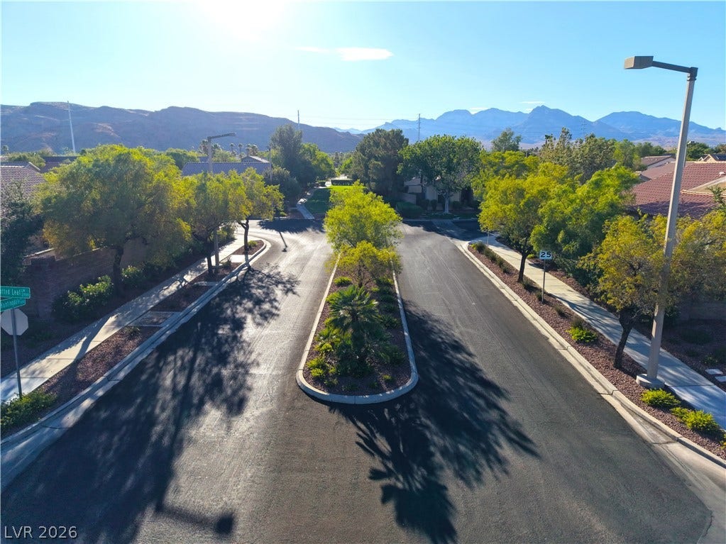 A quiet neighborhood street featuring mature trees, well-maintained sidewalks, and distant mountain vistas.
