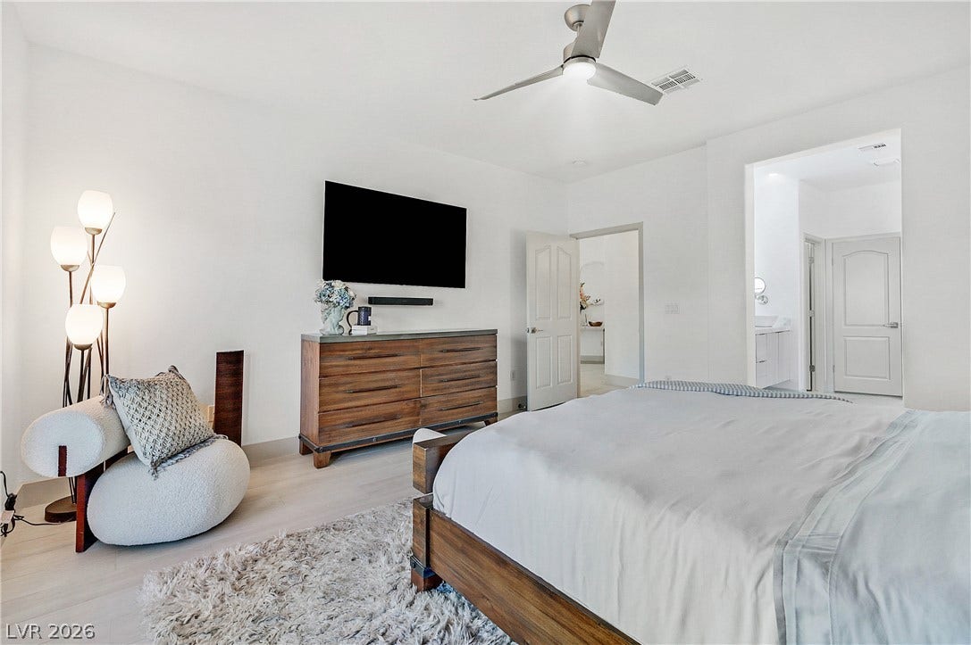 A tranquil bedroom features a ceiling fan, light wood floors, and a well-lit pathway to an adjoining bath.
