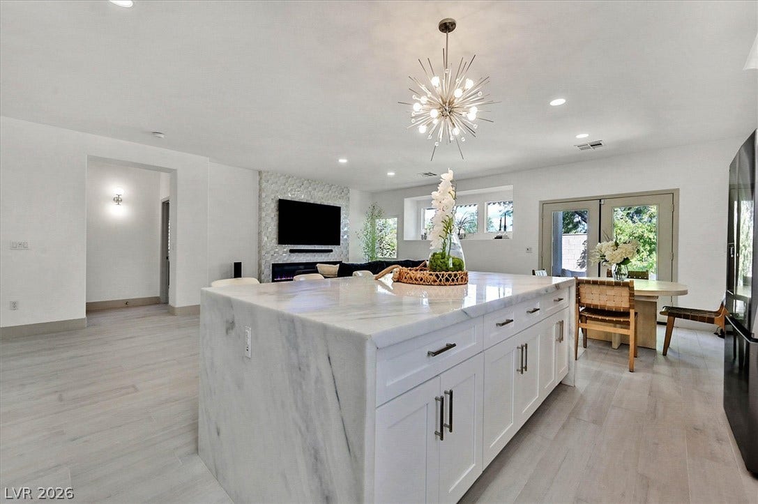 A spacious kitchen features a grand island that lights up, seamlessly connecting to an inviting living area with a textured fireplace wall.
