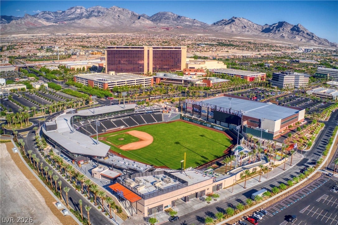 An aerial perspective reveals a vibrant baseball park surrounded by urban amenities and distant mountains.