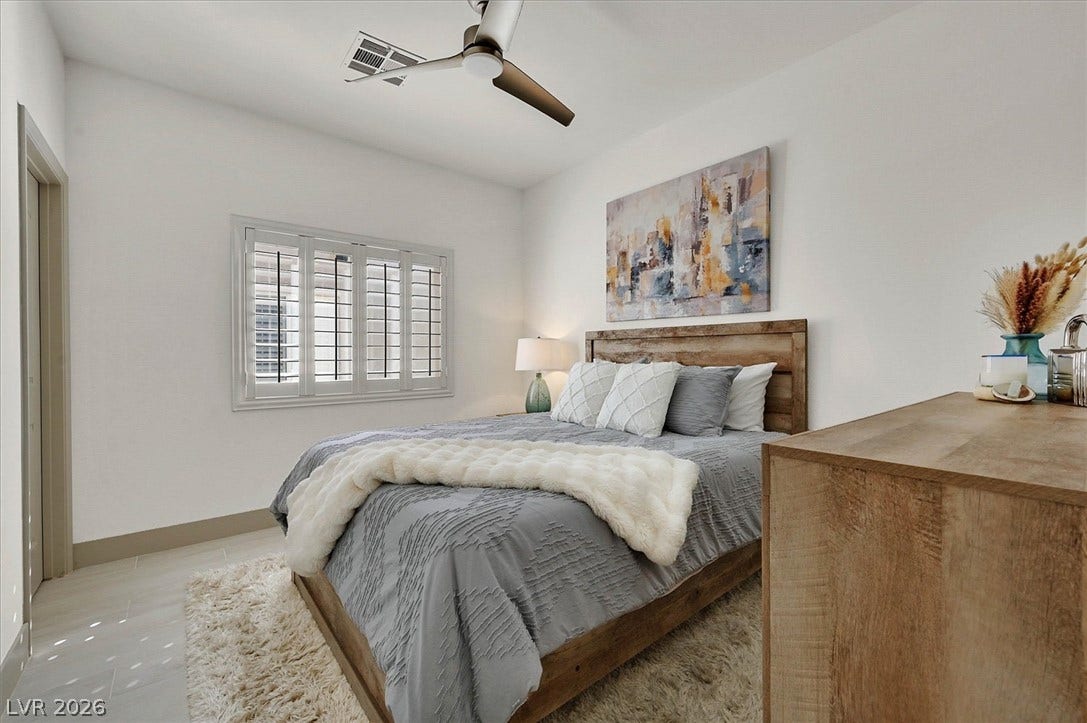 Recessed lighting and a ceiling fan illuminate this well-lit bedroom with a window featuring plantation shutters.