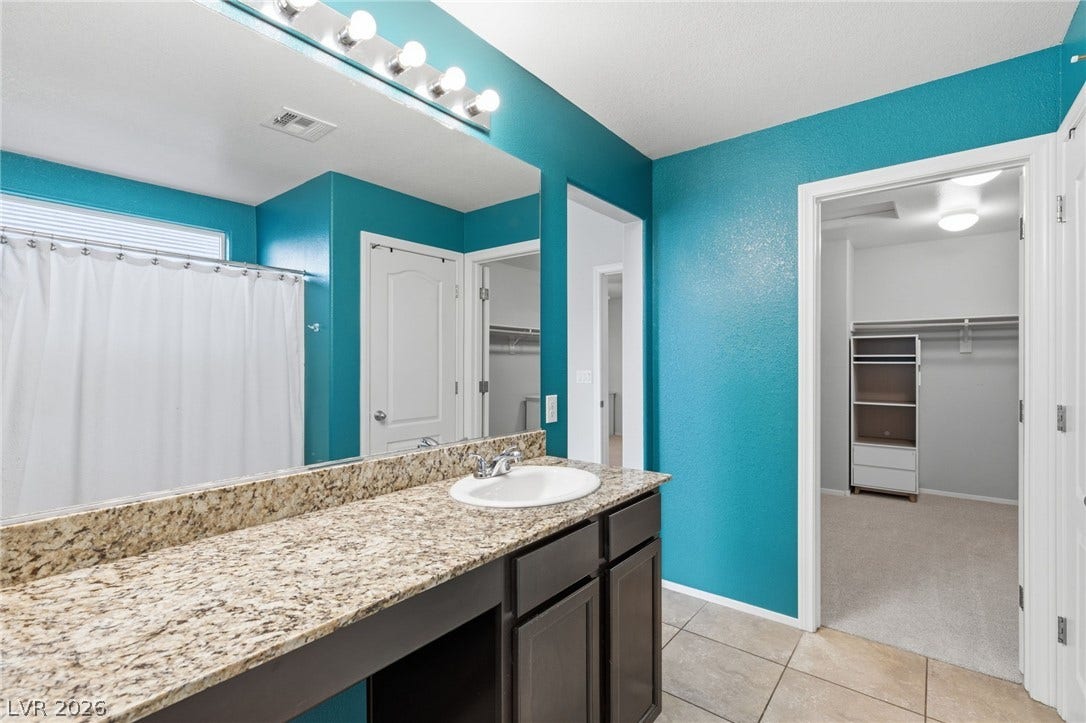 Granite counters and tiled flooring appoint this well-maintained bathroom, offering ample vanity space and access to an adjacent closet.