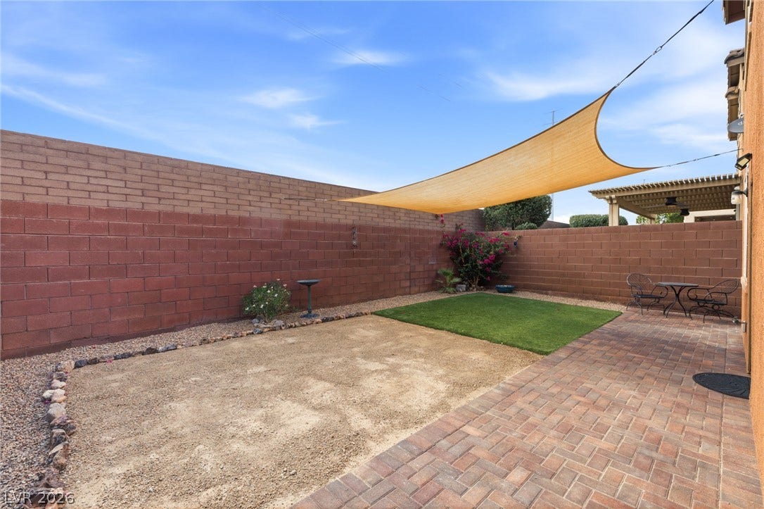 An inviting backyard space features a paved patio, a sun shade, and low-maintenance landscaping for comfortable outdoor living.