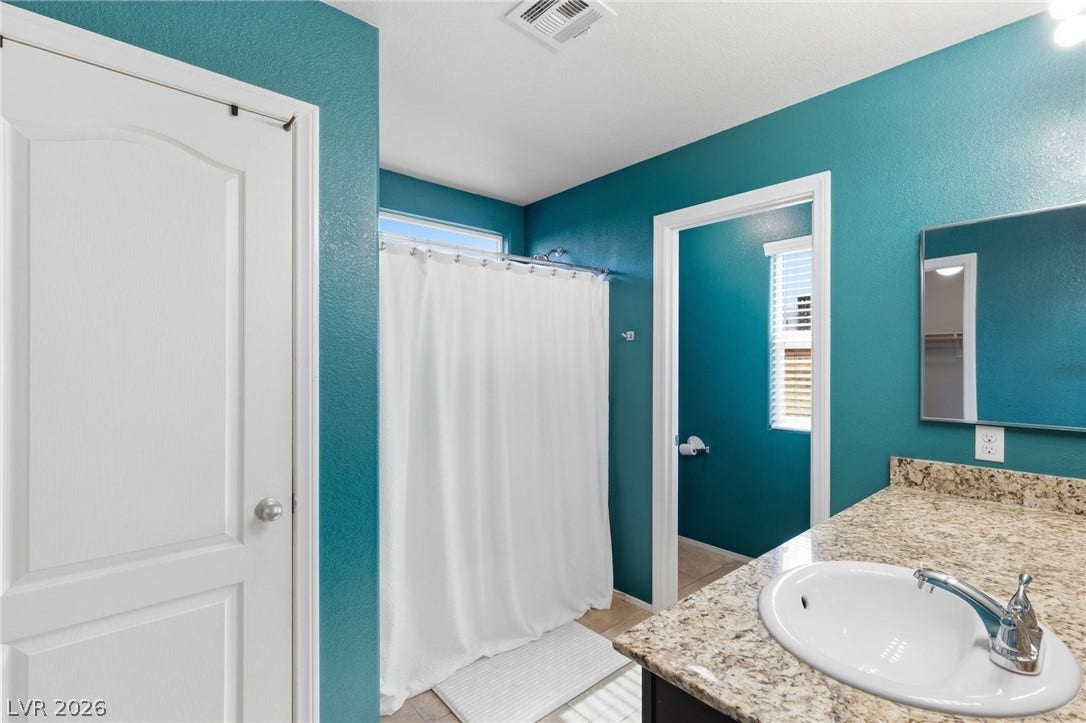 A well-appointed bathroom features a single vanity with stone counters and a shower with a privacy curtain.