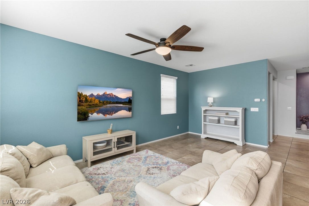 A well-lit living area features tiled flooring, a prominent ceiling fan, and blinds covering the window.